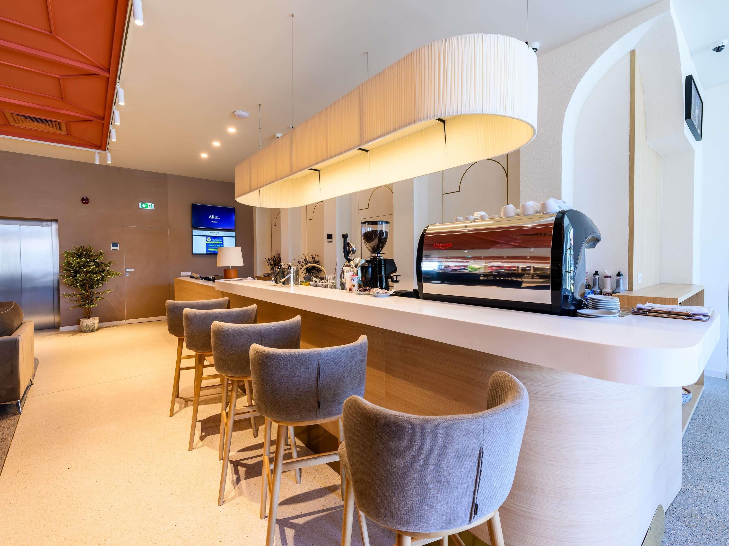 Un área de bar moderna con una máquina de café, asientos y una pantalla de televisión.