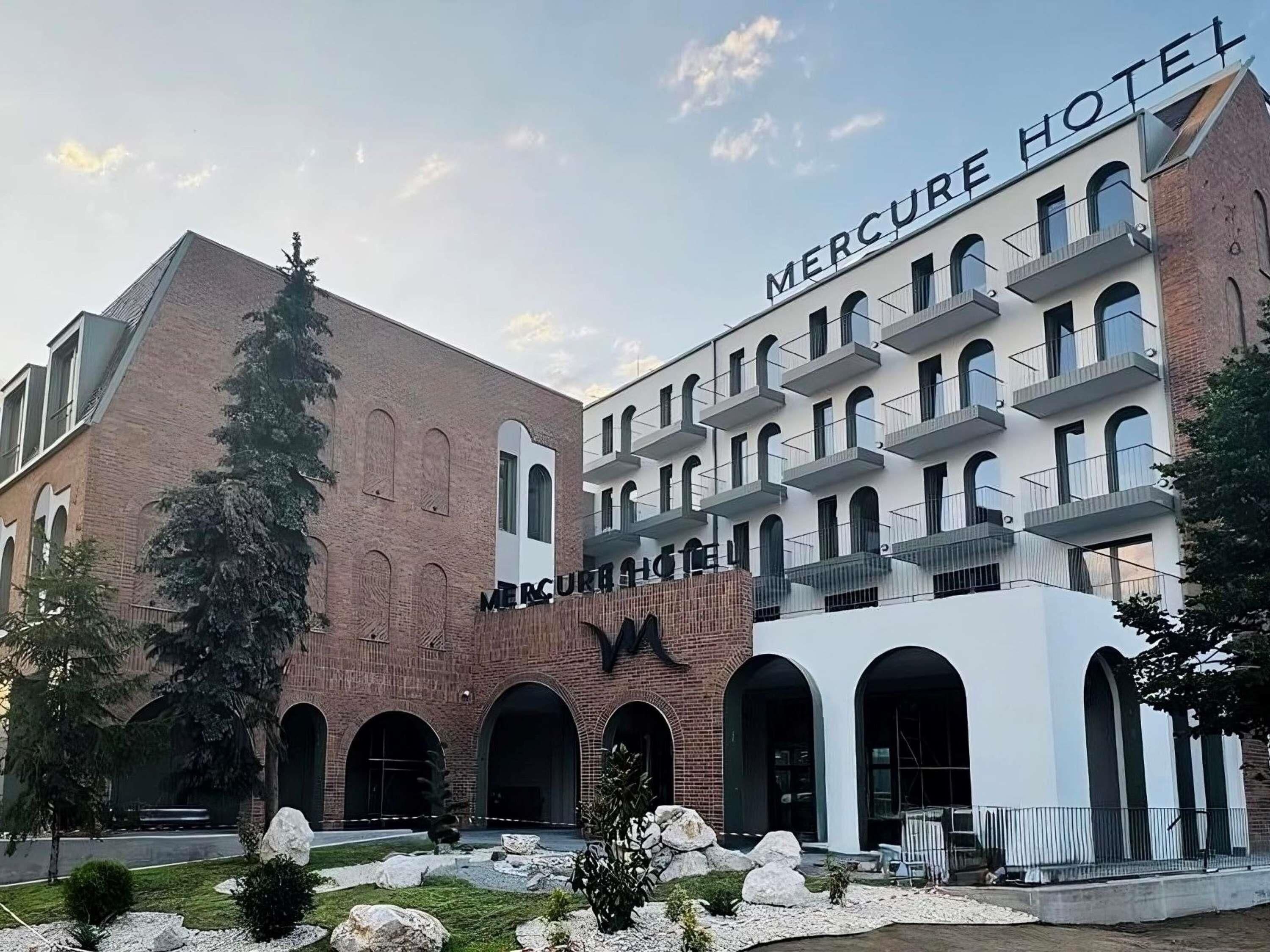 Un hotel con fachada moderna, varios balcones y un patio ajardinado.