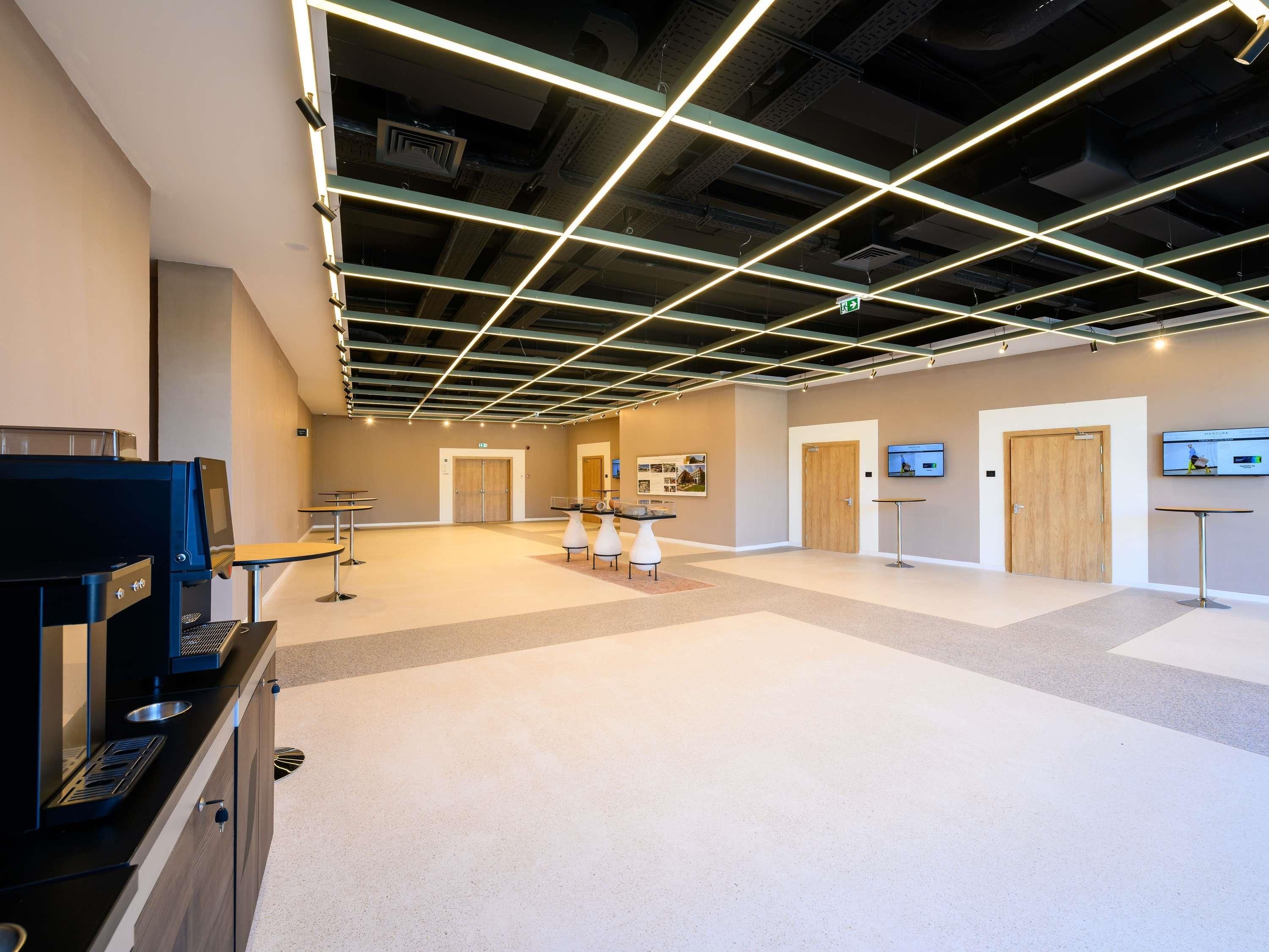 A spacious lobby with a modern ceiling design, a reception area, and a television screen.