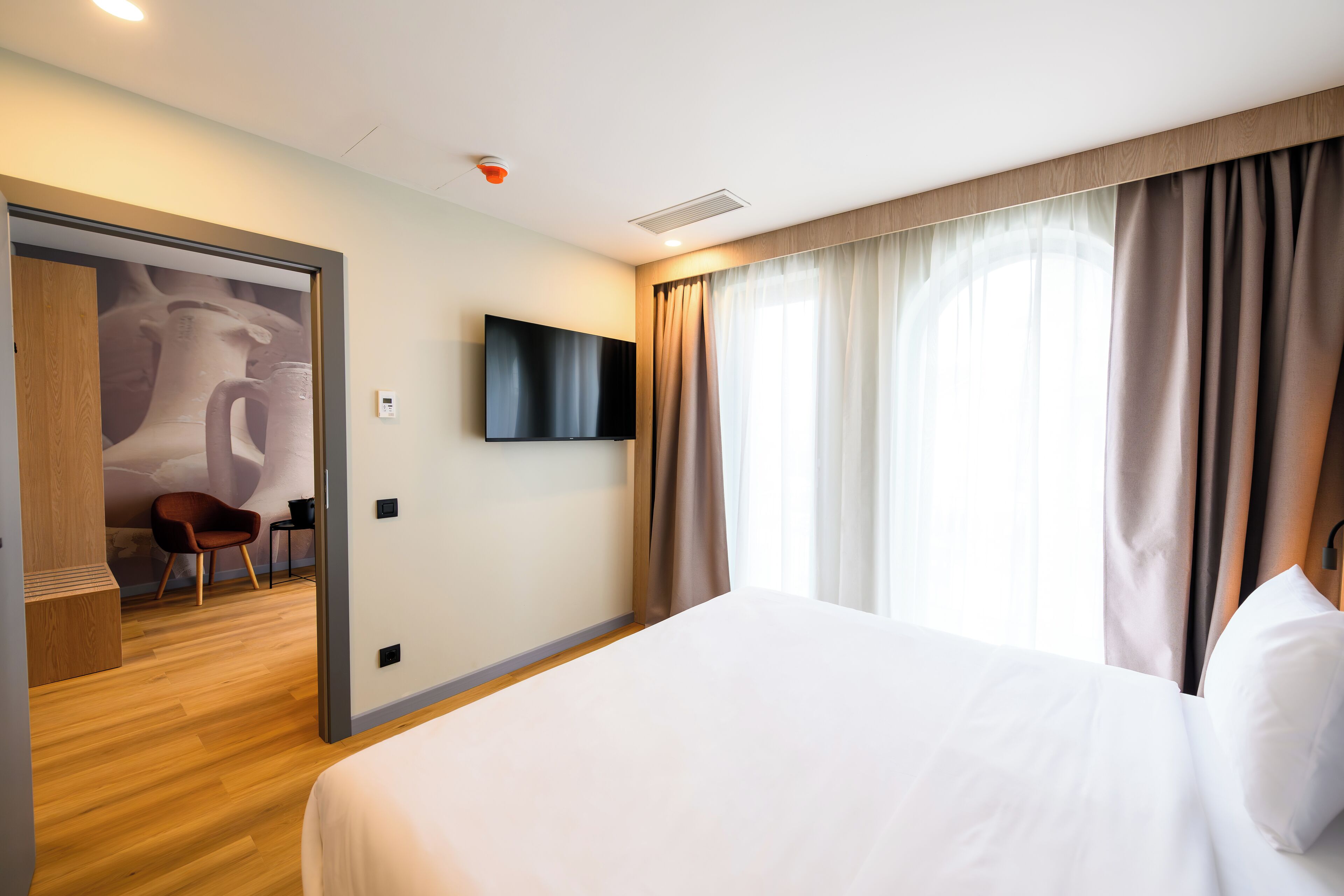 Habitación de hotel con una cama grande, un televisor de pantalla plana, una silla de madera y una puerta que da a un baño.