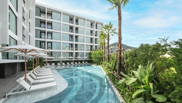 Un hotel moderno con piscina, lettini e palme.