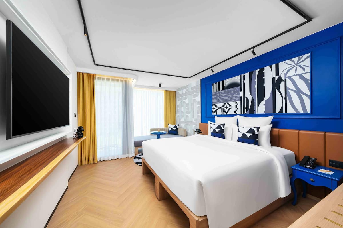 A modern hotel room with a large bed, a flat-screen TV, a desk, and a blue accent wall.