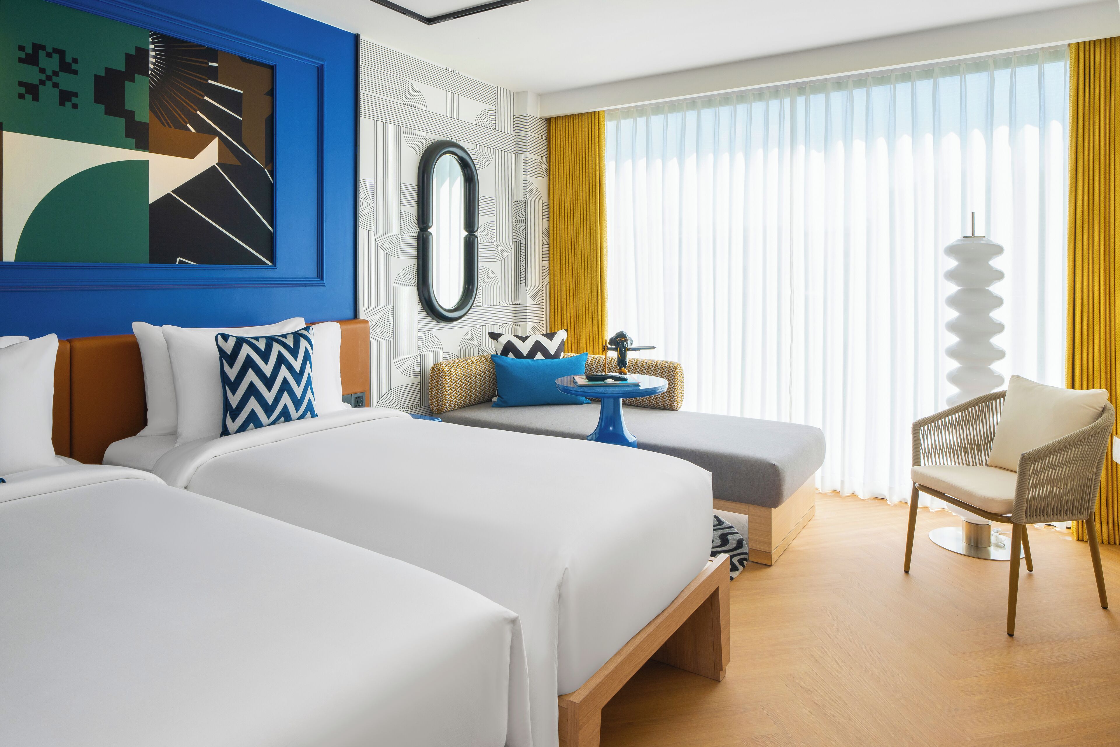 Ein Hotelzimmer mit zwei Betten, einem Schlafsofa, einem kleinen Tisch und einem Stuhl.