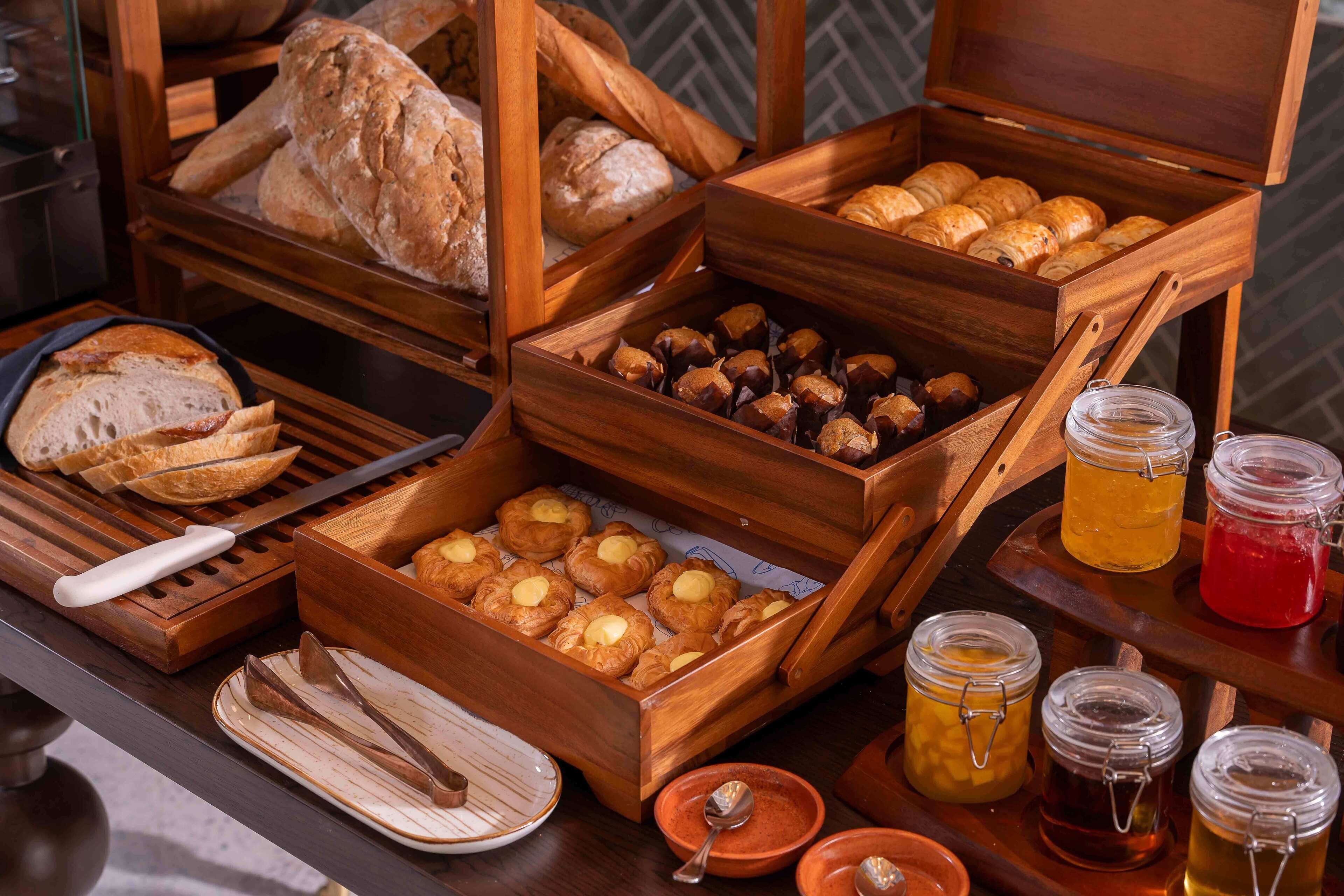 A breakfast buffet with various breads, pastries, and jams.