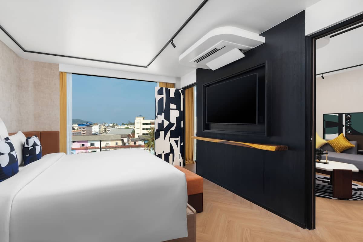 A modern hotel room with a large bed, a flat-screen TV, a city view, and a balcony.
