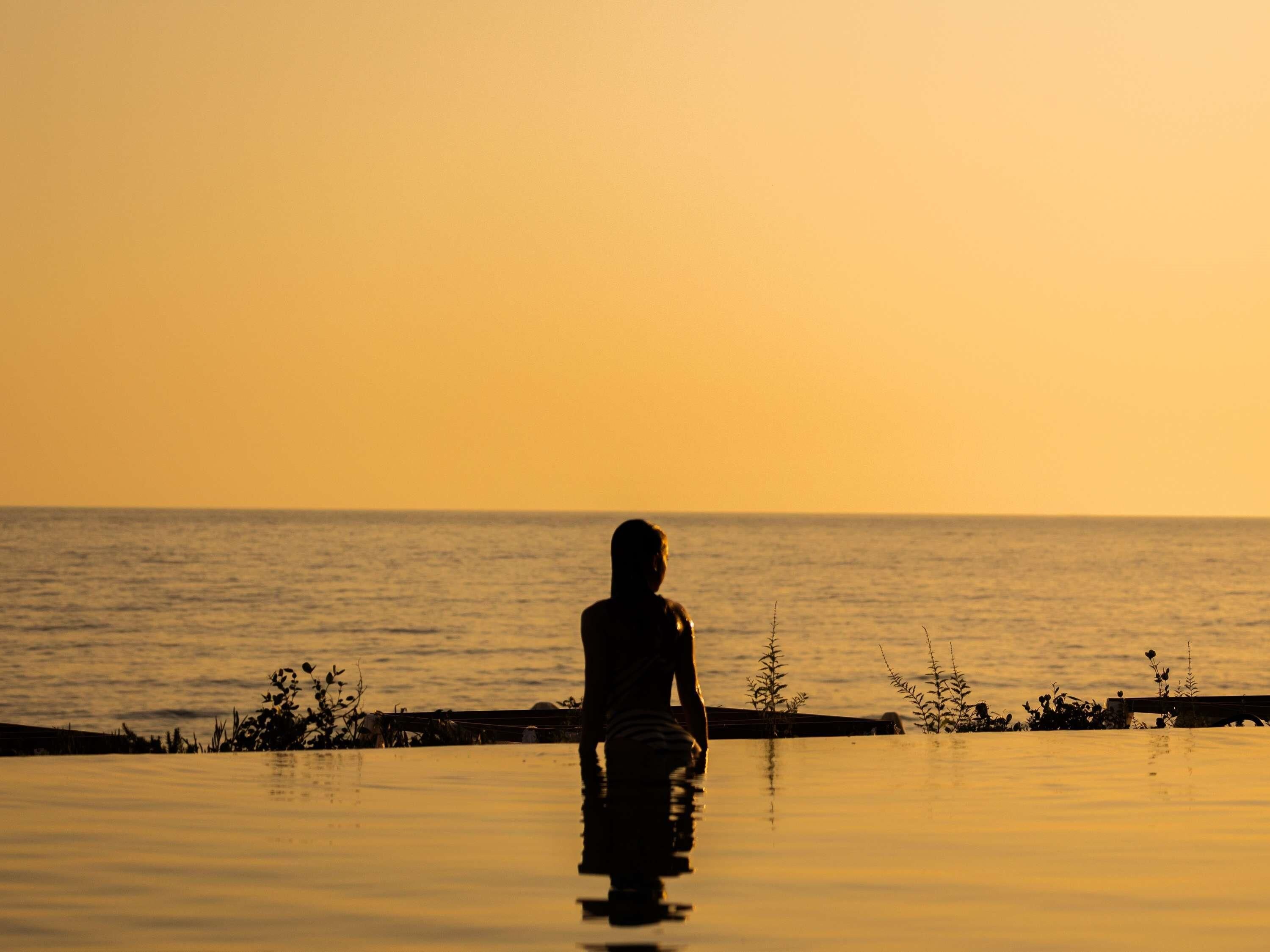Una persona sentada junto al agua durante el atardecer.