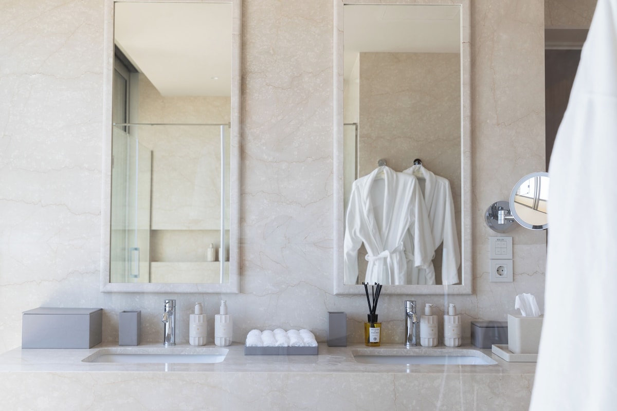 A bathroom with two sinks, a large mirror, and a robe hanging on a hook.