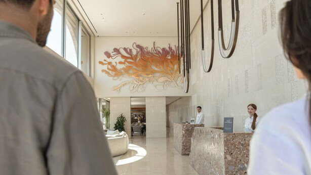 A hotel reception area with a marble reception desk, a large floral wall art piece, and a seating area with a sofa.