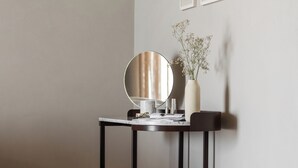 Quarto minimalista com espelho redondo, uma pequena mesa, um vaso com flores e um banquinho marrom.