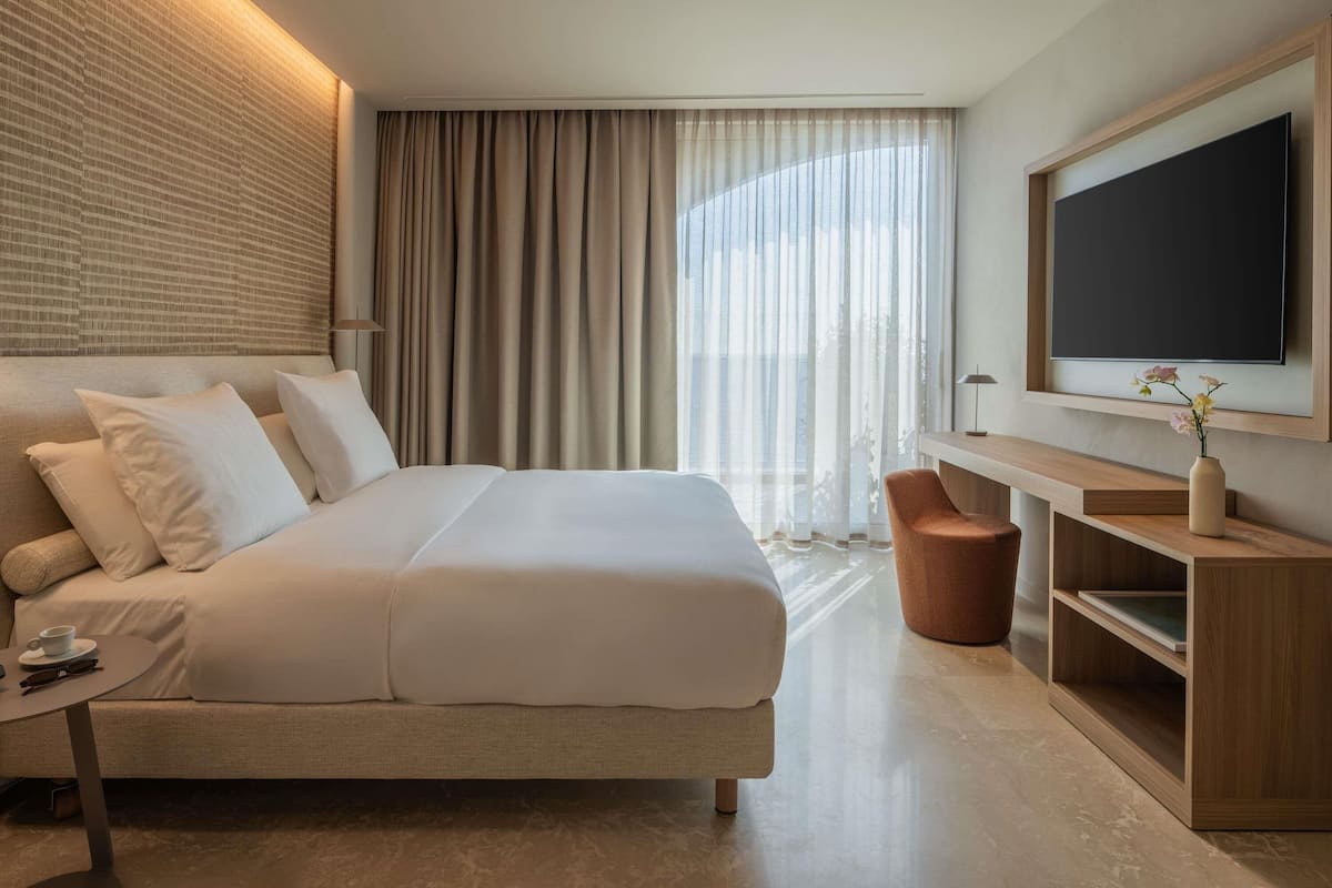Ein modernes Hotelzimmer mit einem großen Bett, einem Schreibtisch, einem Fernseher und Blick ins Freie.
