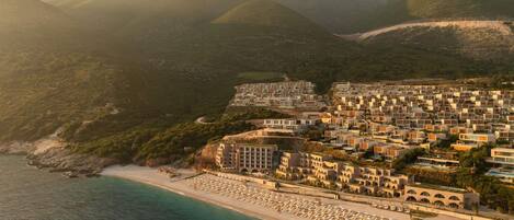 A coastal town with a beach, buildings, and mountains.