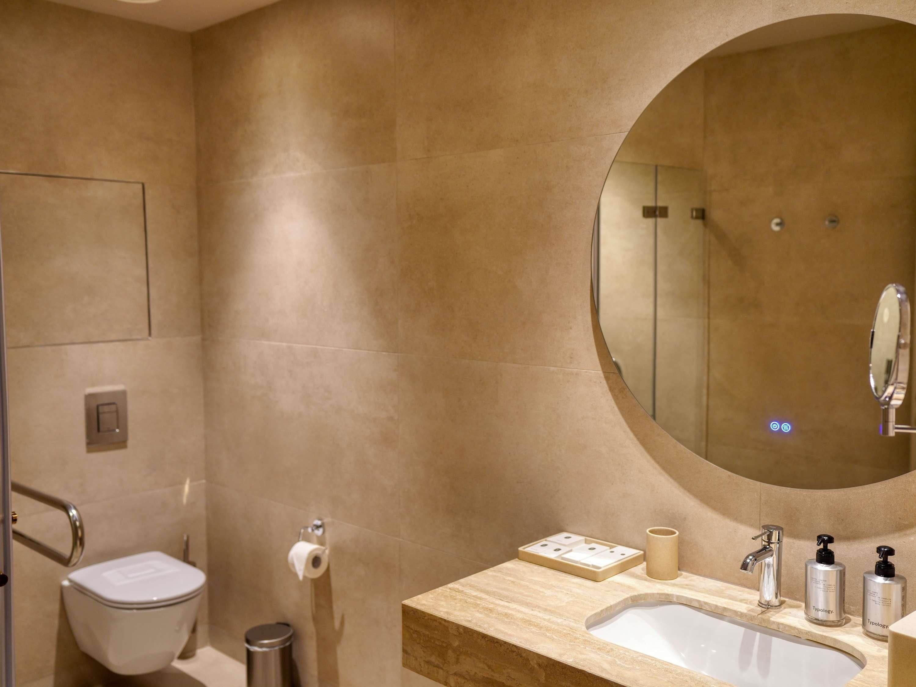 Een moderne badkamer met toilet, wastafel, spiegel en prullenbak.