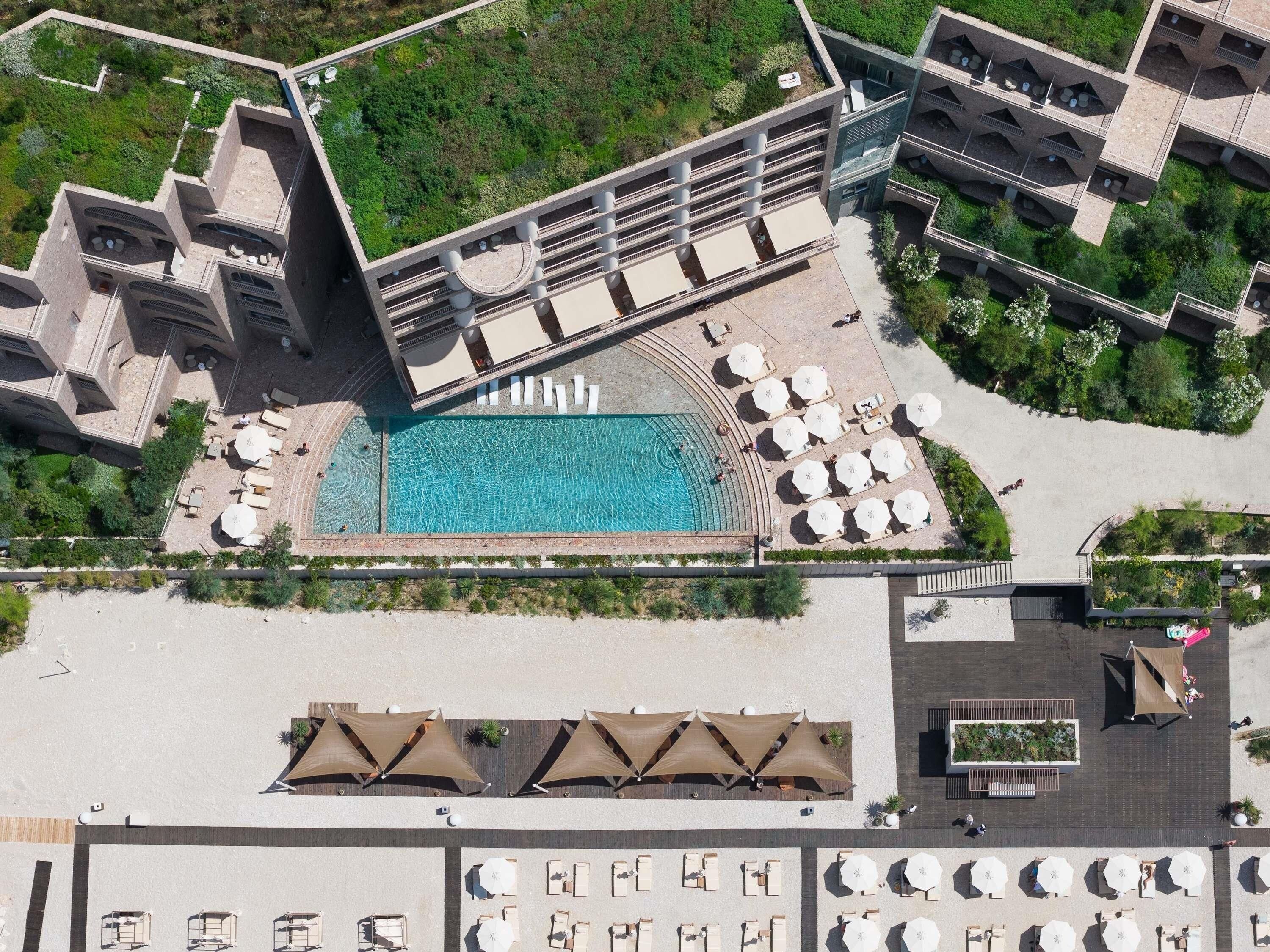 Vista aérea de un hotel con piscina central, zonas de estar exteriores y un jardín ajardinado.