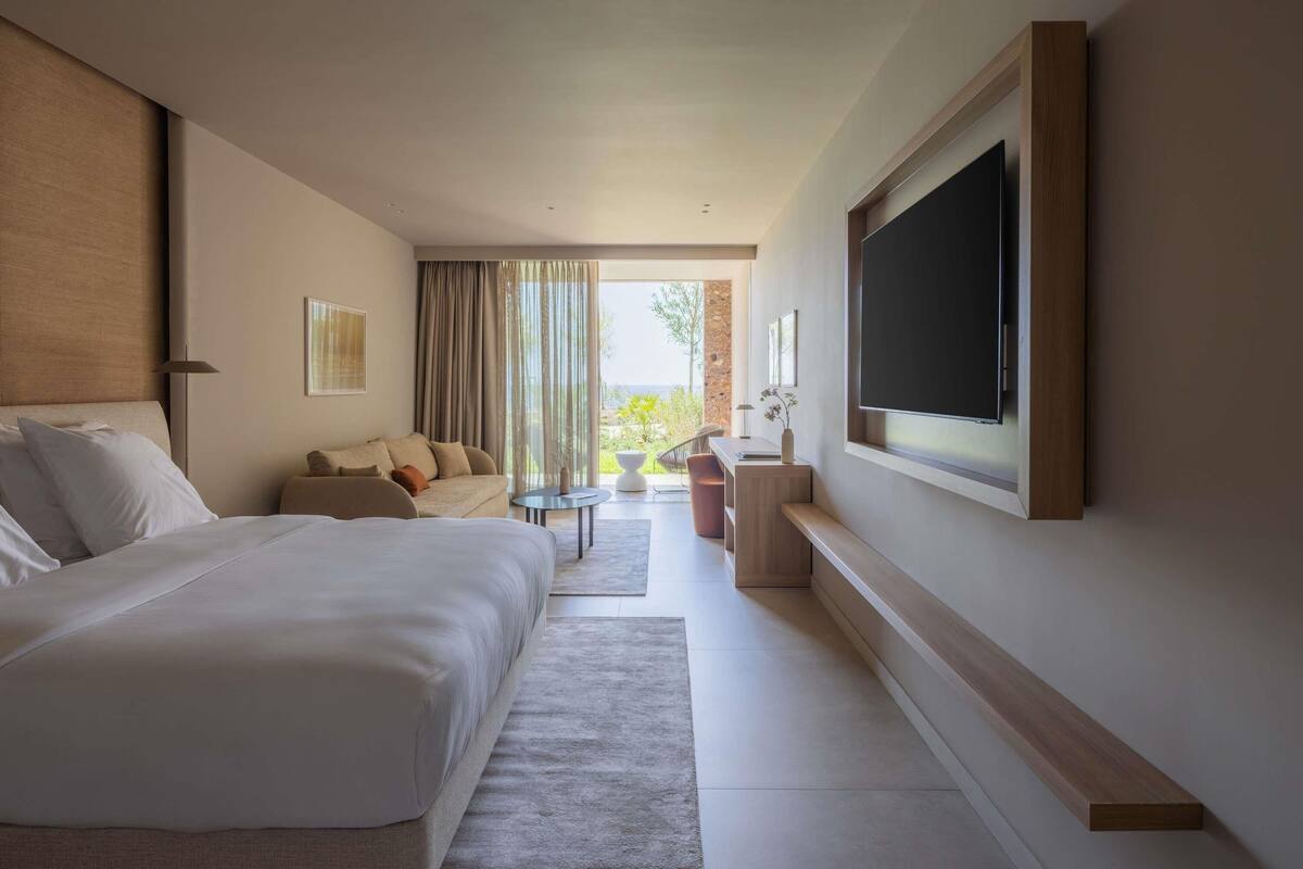 Ein modernes Hotelzimmer mit einem großen Bett, einer Couch, einem an der Wand montierten Fernseher und einem kleinen Tisch mit einer Vase.