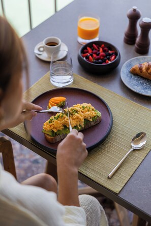 A dining table with a plate of food, a glass of orange juice, and a bowl of berries. - Green Coast Hotel Mgallery Collection (Himare)