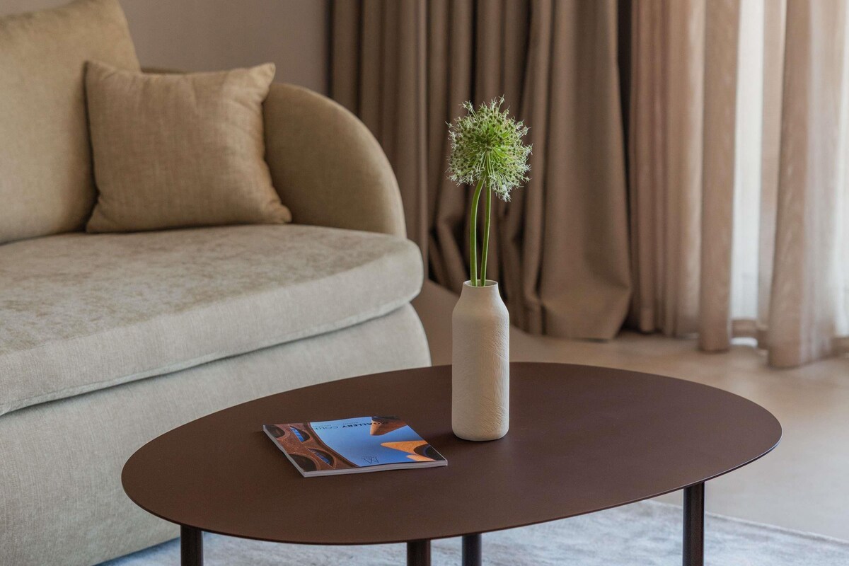 A living room with a sofa, a coffee table, a vase with flowers, and a magazine.