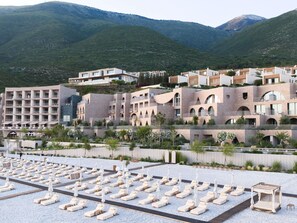 A resort with multiple buildings, a pool area with sun loungers, and a mountainous backdrop.