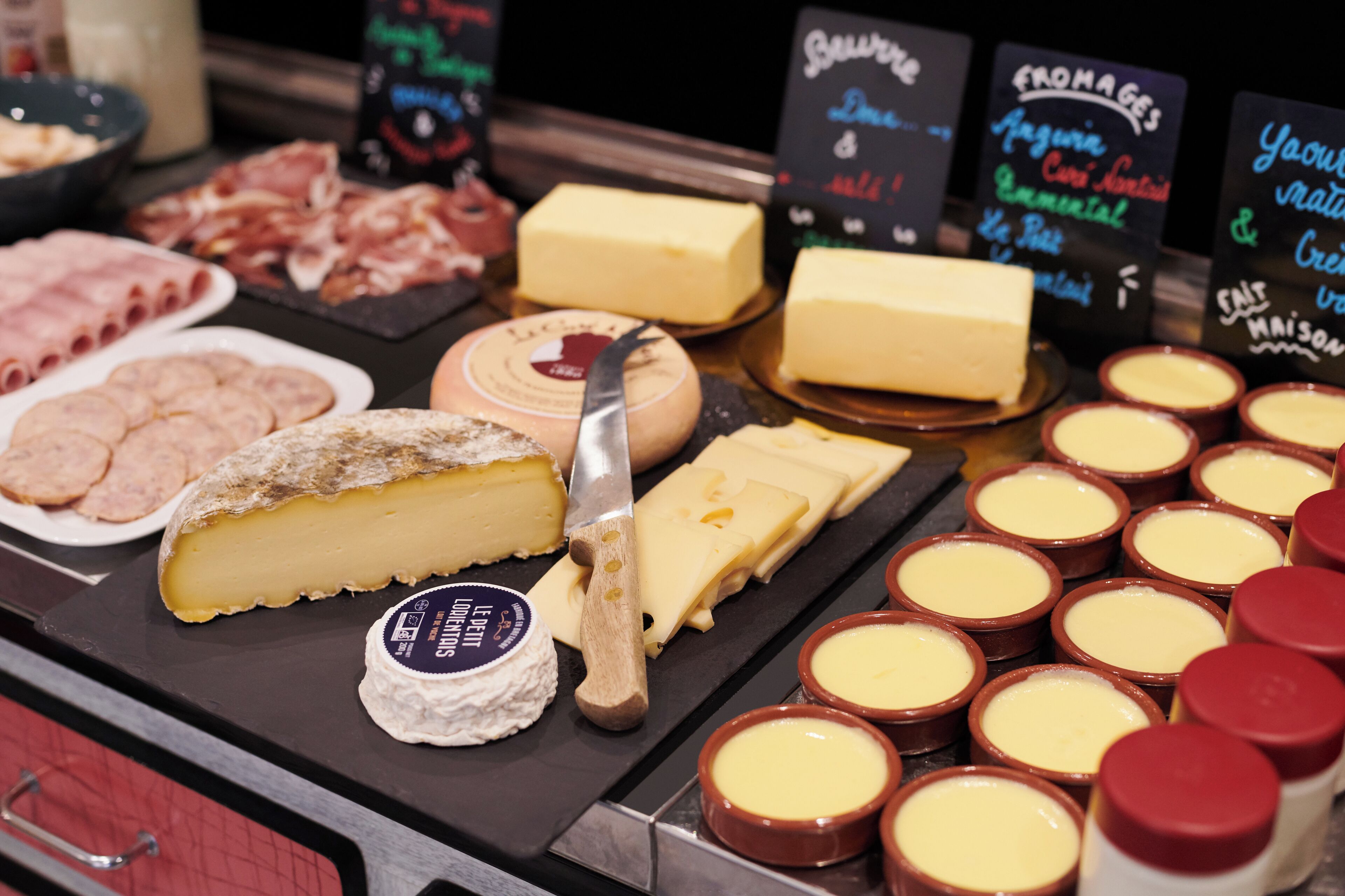Una exhibición de quesos y embutidos con diversas variedades de queso, incluyendo un queso grande en rueda y bloques más pequeños, junto a varios tipos de carne curada.