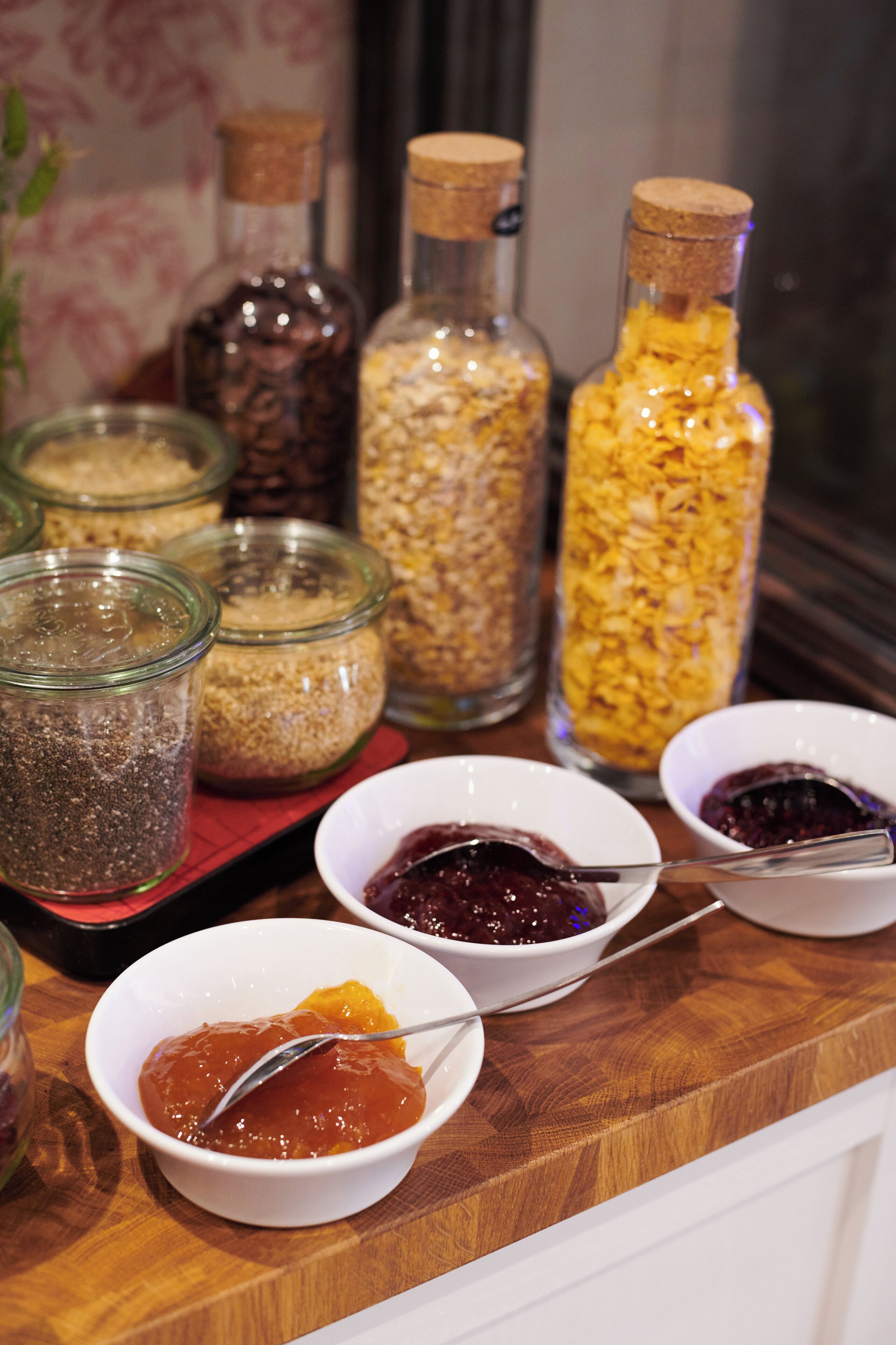 Una mesa de madera con botes de vidrio que contienen diferentes alimentos y pequeños cuencos con salsas y untables.