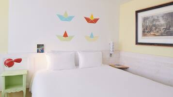 A hotel room with a bed, pillows, a bedside table with a lamp, a framed picture on the wall, and origami boats on the wall.