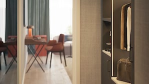 A modern interior with a dark-toned wardrobe, a dining area with a table and chairs, and a view through an open doorway.