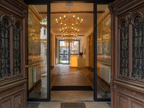 Une entrée imposante, ornée de portes en bois sculptées, dotée d’un sol à motifs et surmontée d’un lustre moderne.