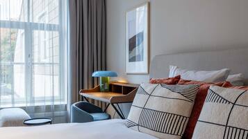 A hotel room with a bed, a desk, a chair, a lamp, and a window with curtains.