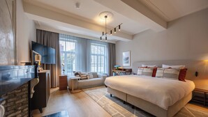 Ein modernes Hotelzimmer mit einem großen Bett, einem Flachbildfernseher, einem Schreibtisch und einem großen Fenster mit Vorhängen.