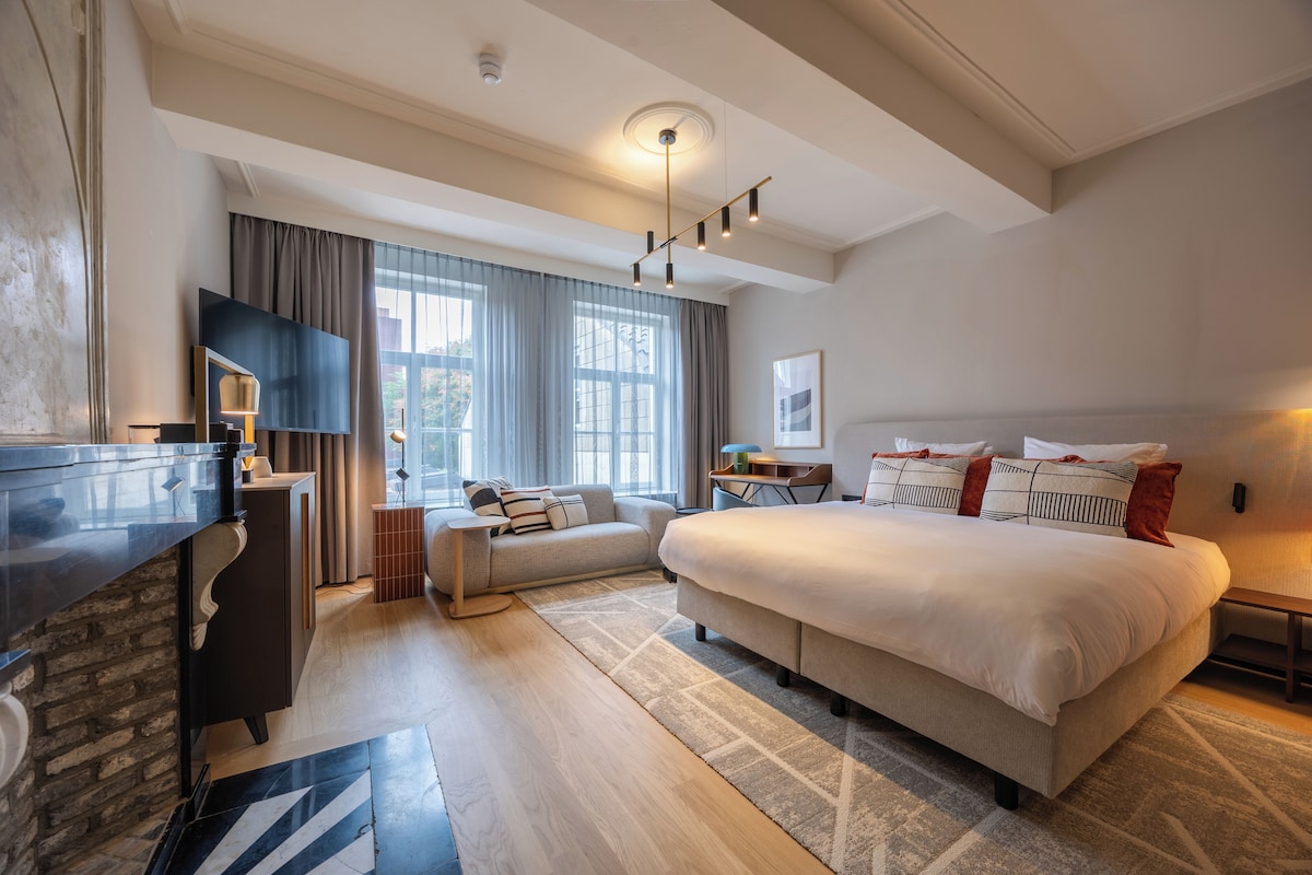 Une chambre d’hôtel moderne dotée d’un grand lit, d’un téléviseur à écran plat, d’un bureau et d’une grande fenêtre avec des rideaux.