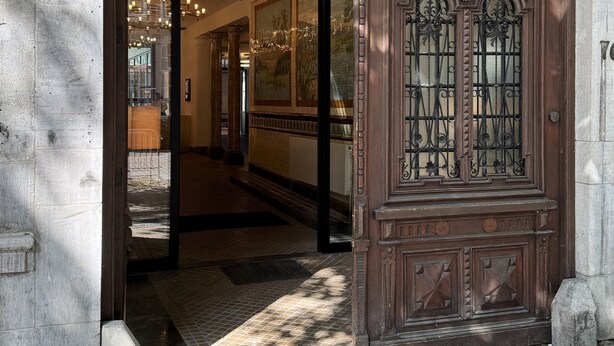 An arched entrance with a wooden door featuring intricate metalwork and a glass panel.