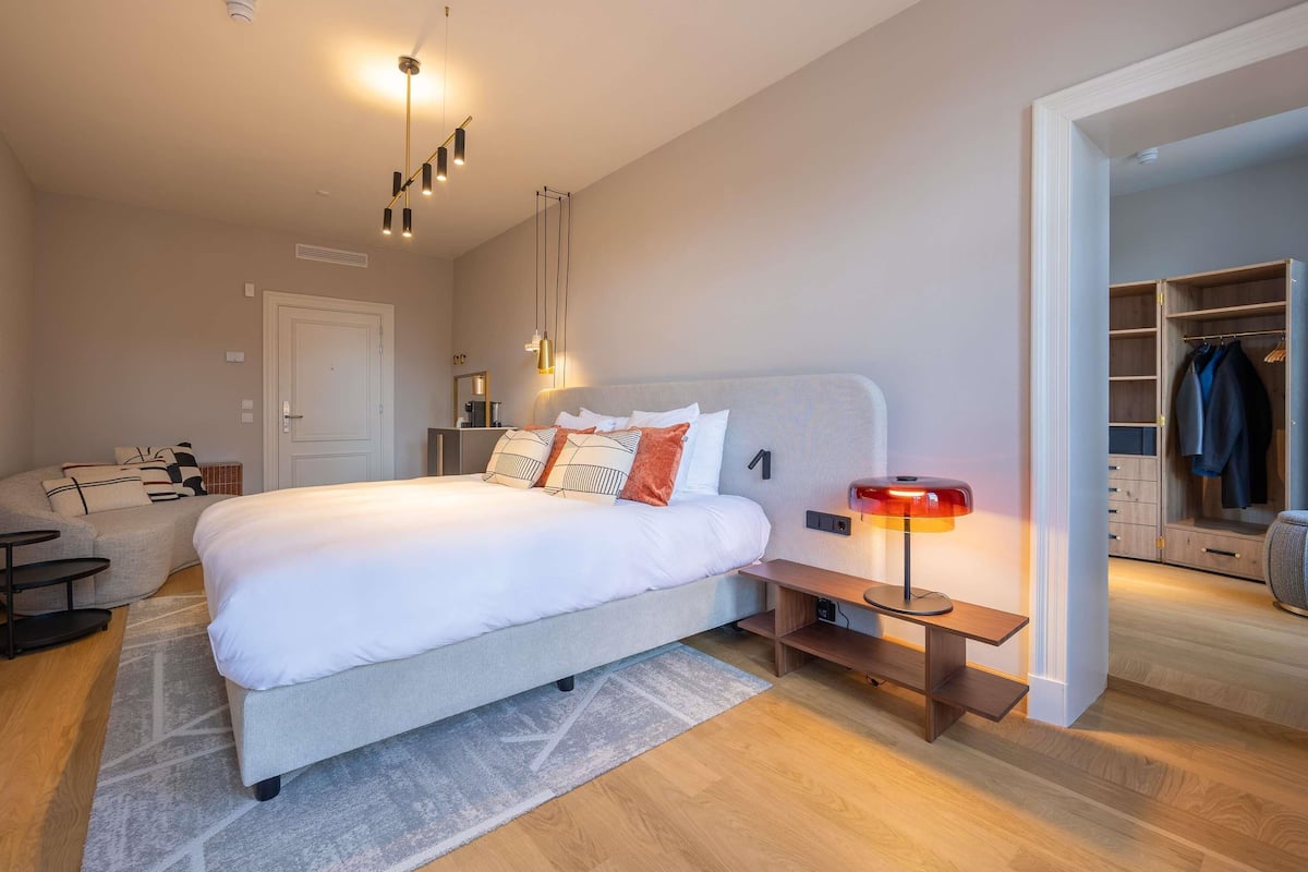 Een moderne slaapkamer met een groot bed, nachtkastjes, een garderobe en een bureau.