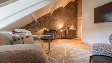 A loft-style living space with a sloped ceiling, exposed brick wall, and a flat-screen TV mounted on the wall.
