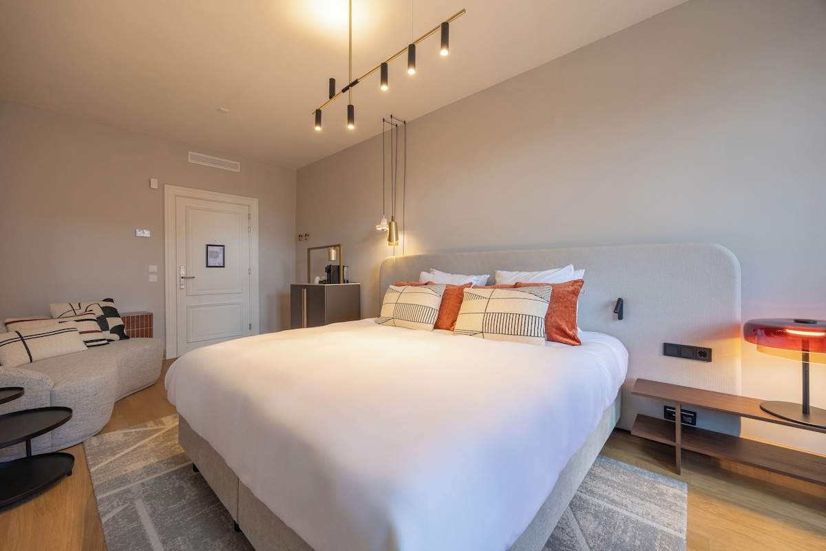 Une chambre d’hôtel moderne, dotée d’un grand lit, d’un canapé, d’un bureau et d’une table de chevet avec une lampe.