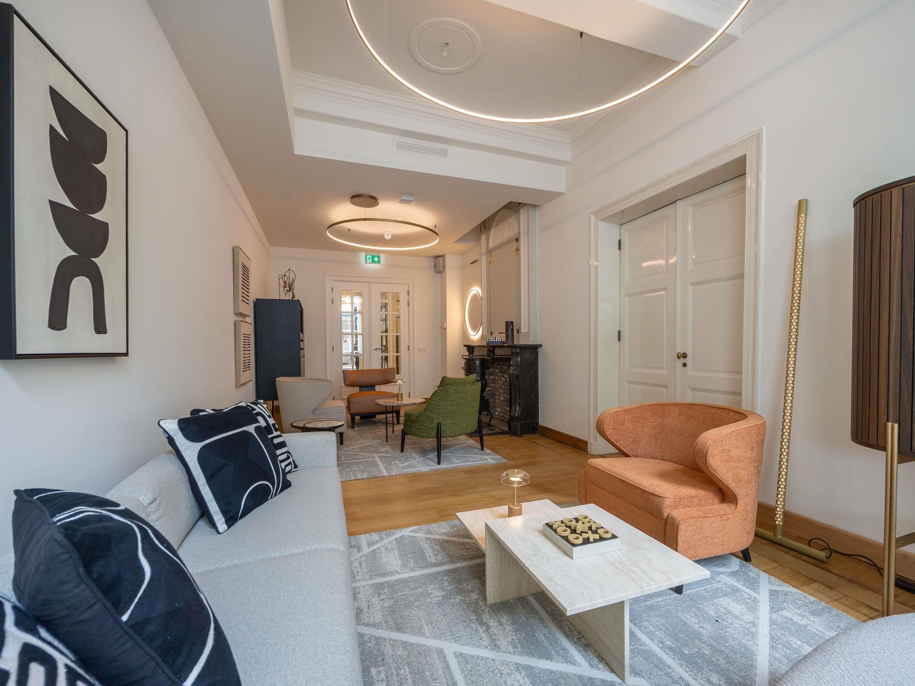 A modern hotel lobby with a sofa, armchairs, a coffee table, and a fireplace.