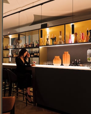 A bar area with shelves of bottles, a counter, and a person seated. - Hotel Maison Maastricht Centrum - Handwritten Collection (Maastricht)