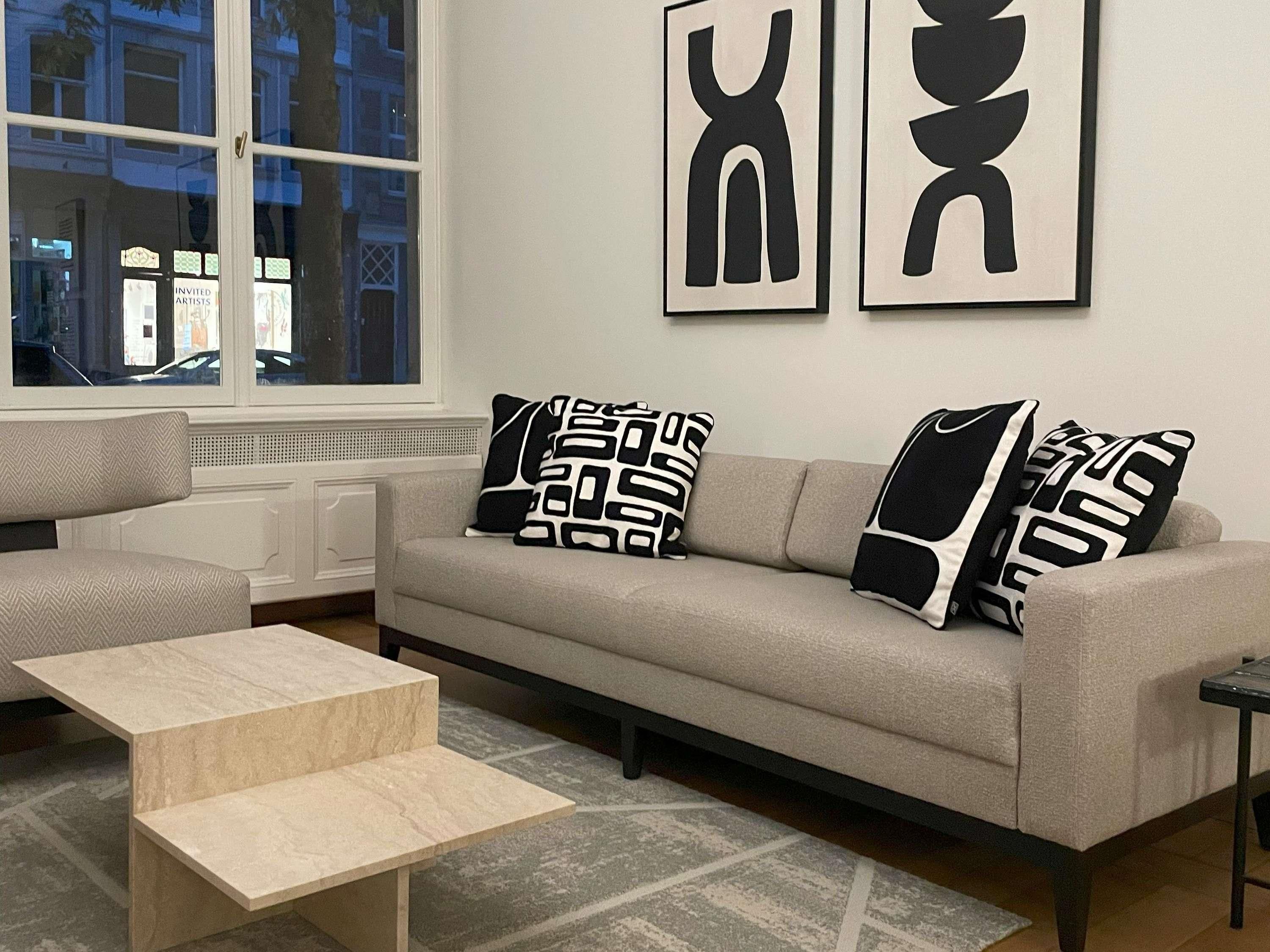 Ein modernes Wohnzimmer mit einer Couch, zwei schwarz-weiß gemusterten Kissen, einem kleinen Holztisch und abstrakter Wandkunst.