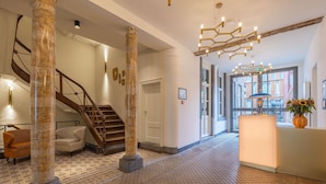 A spacious lobby with a marble column, a wooden staircase, and a modern chandelier.
