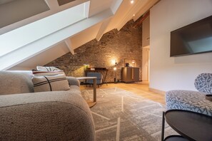 Een loft-achtige kamer met een schuine plafond, een zichtbare bakstenen muur en een flatscreen televisie aan de wand.