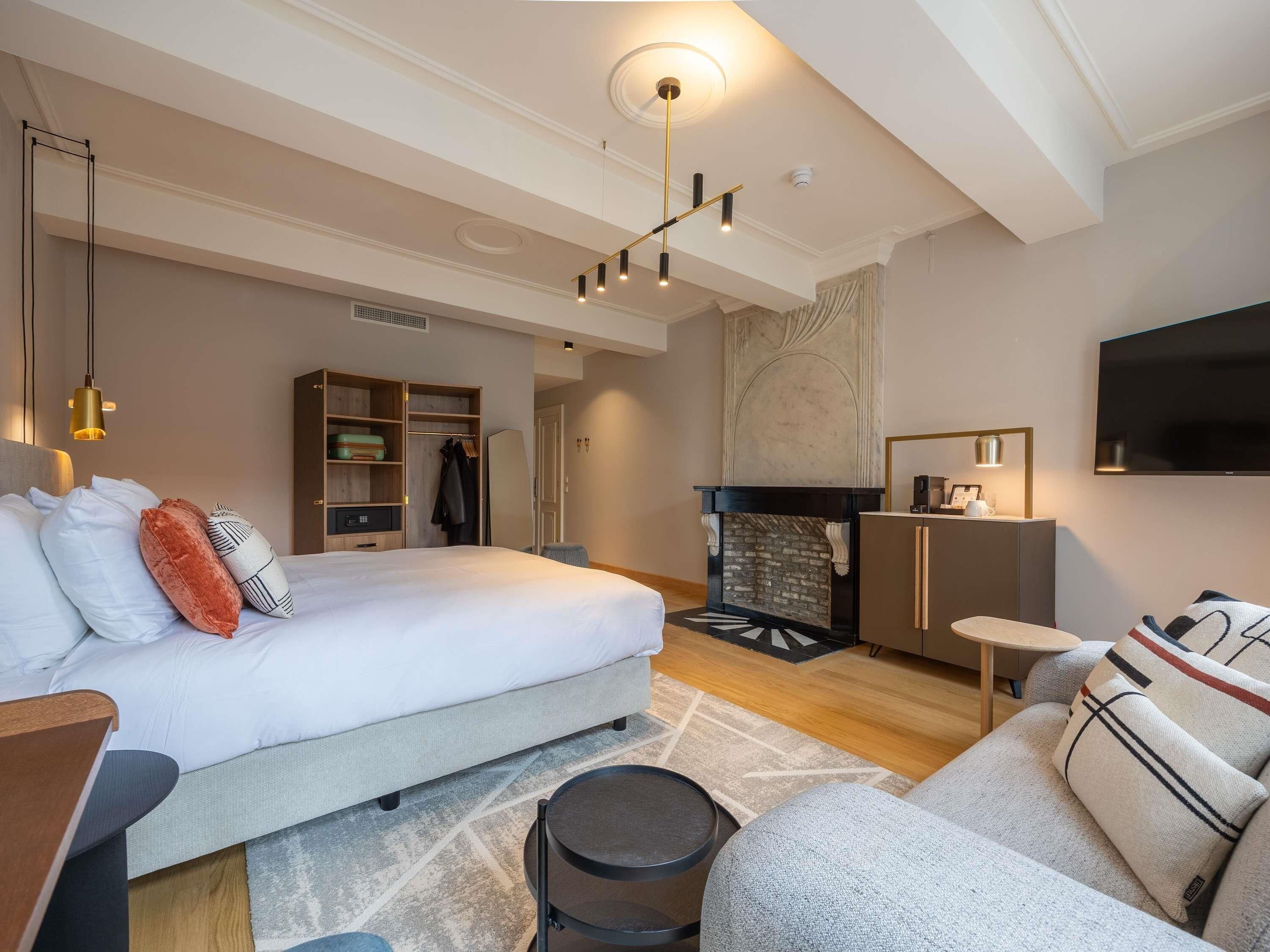 A modern hotel room with a large bed, a fireplace, a television, and a seating area.
