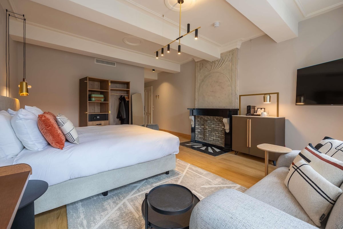 Een moderne hotelkamer met een groot bed, een open haard, een televisie en een zithoek.