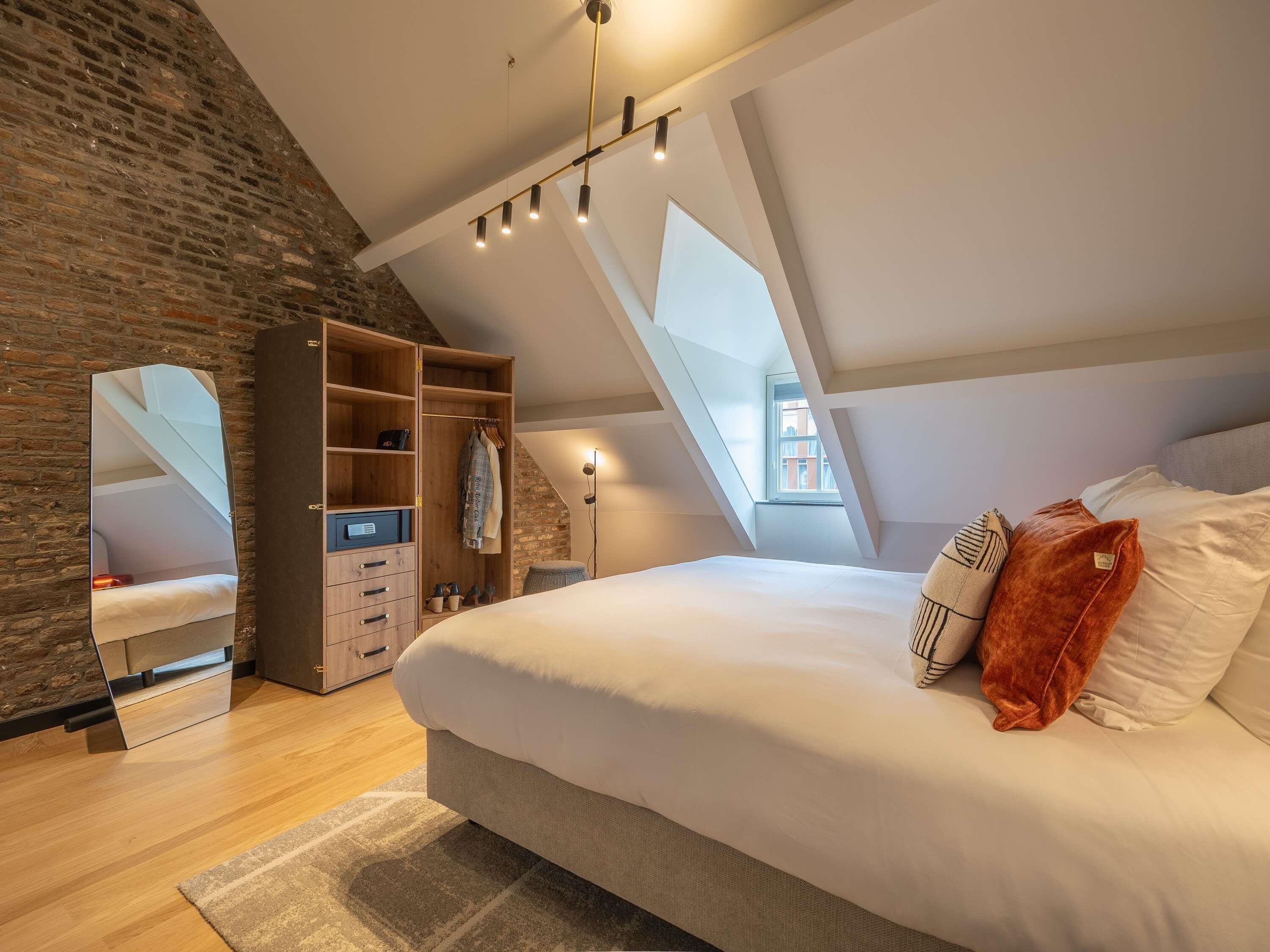 A bedroom with a loft-style ceiling, a large bed, a wardrobe, and a mirror.