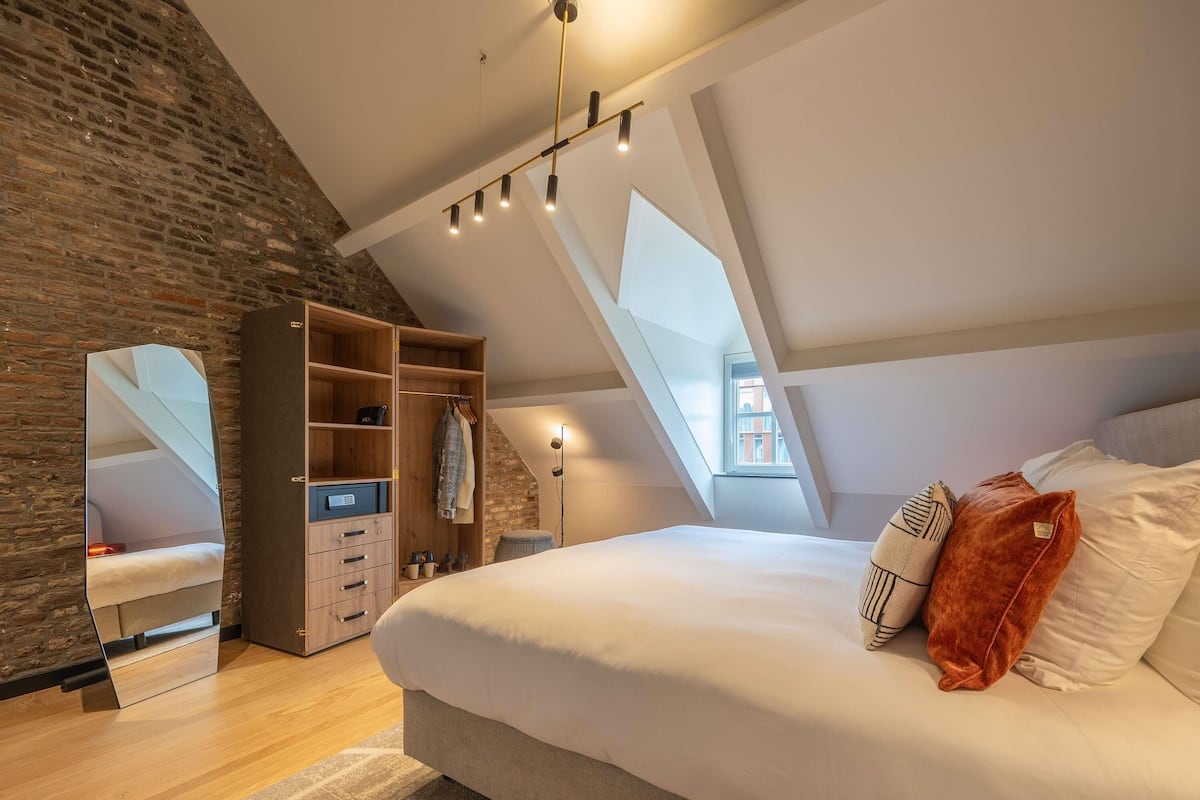 Een slaapkamer met een loft-plafond, een groot bed, een kledingkast en een spiegel.