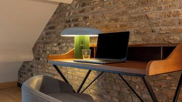 A laptop on a desk with a lamp, a chair, and a brick wall.