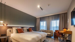 A modern hotel room with a large bed, a desk, a chair, and a sofa.