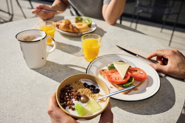 A breakfast setting with a bowl of cereal, a plate with toast and tomatoes, a croissant, and a glass of orange juice. - ibis Madrid Norte Las Tablas (Madrid)