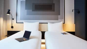 Una habitación de hotel con dos camas, una laptop sobre una cama y una revista sobre la otra.