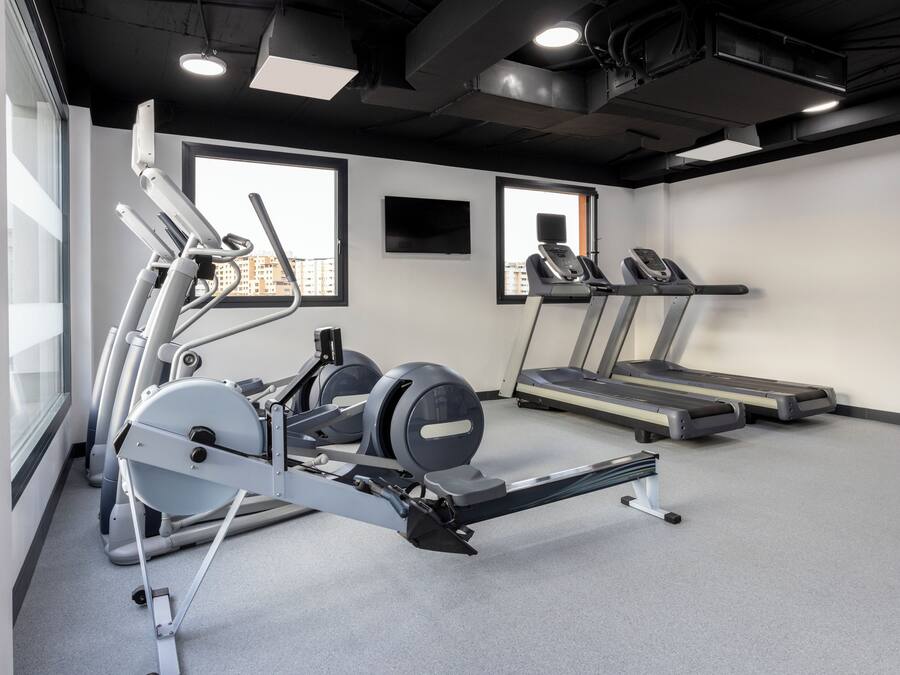 Uma academia com aparelhos de ginástica cardiovascular, esteiras e remo.