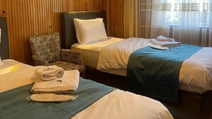 A hotel room with two beds, a wooden panel wall, a wall-mounted light, and a window with sheer curtains. - EL'A APART HOTEL (Camlihemsin)
