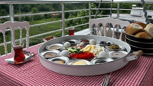 A table with a checkered tablecloth, a tray of food, and a view of green hills in the background. - EL'A APART HOTEL (Camlihemsin)