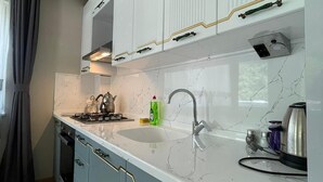 A modern kitchen with white cabinets, a marble countertop, and a gas stove. - EL'A APART HOTEL (Camlihemsin)